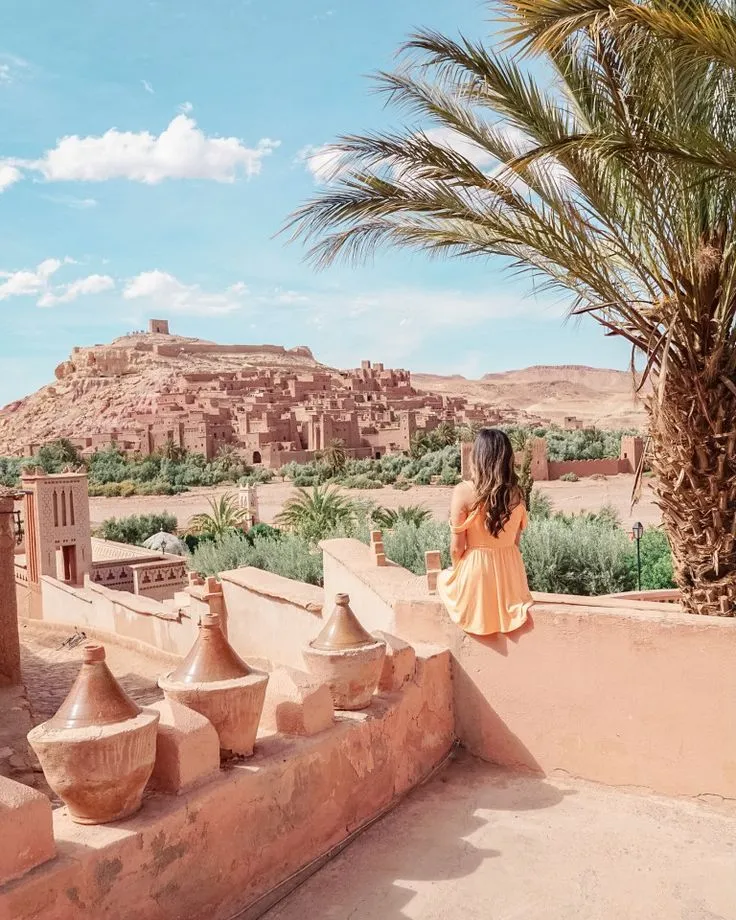 Traveler sitting on a wall looking out over the UNESCO World Heritage site of Ait Ben Haddou near Ouarzazate, Morocco.