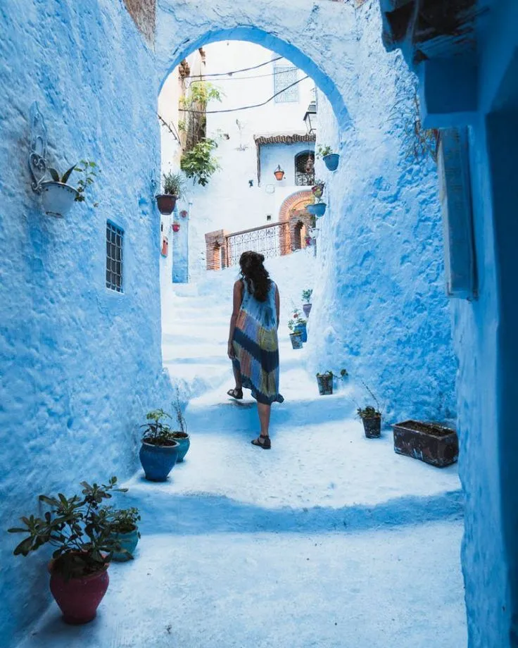 Woman walking through a blue archway and up stairs in the vibrant streets of Chefchaouen, the Blue City.